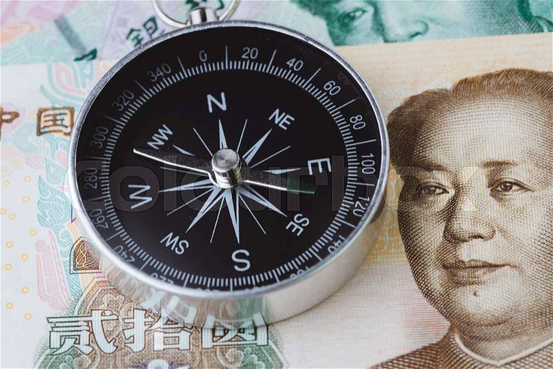 China economy direction slow down impacted by trade war, world emerging market slow growth country concept, closed up of compass on Chinese Yuan banknotes on table, stock photo