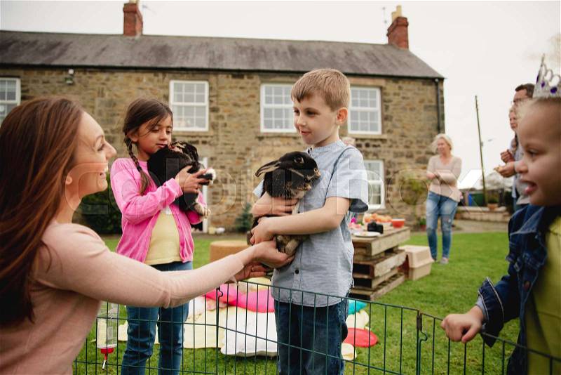 Young boy standing outdoors, a mid adult woman is handing him a bubby rabbit to hold. , stock photo