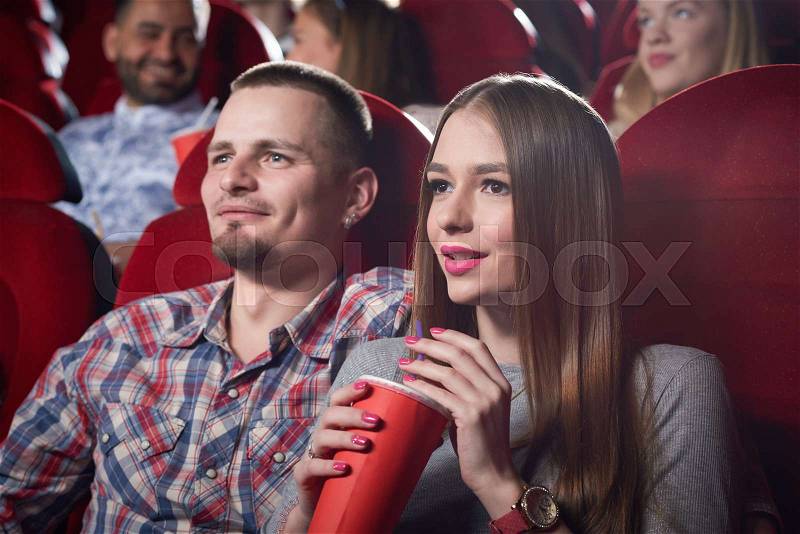 Couple of man in checked shirt and woman in gray sitting together in cinema, watching romantic movie. Handsome bearded man hugging beautiful girlfriend who sitting ..., stock photo