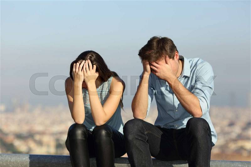 Sad couple complaining after argument sitting outdoors in a city ourskirts, stock photo