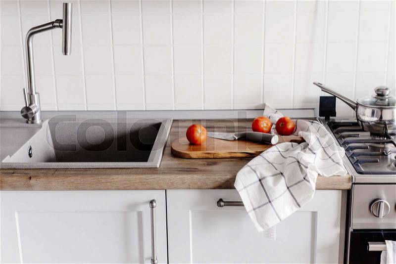 Cooking food on modern kitchen with steel oven, pots, knife on wooden cutting board with vegetables, spices on wooden tabletop at sink with water. Home food. Stylish ..., stock photo