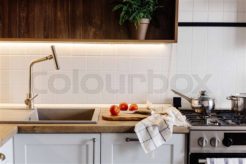 Cooking food on modern kitchen with steel oven, pots, knife on wooden cutting board with vegetables on wooden tabletop at sink with water. Home food. Stylish ..., stock photo