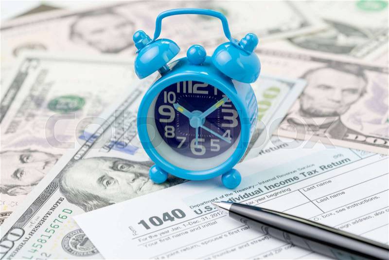 Time or deadline for yearly tax submission concept, miniature small retro alarm clock with pen on 1040 US individual income tax filling form on pile of US dollar ..., stock photo