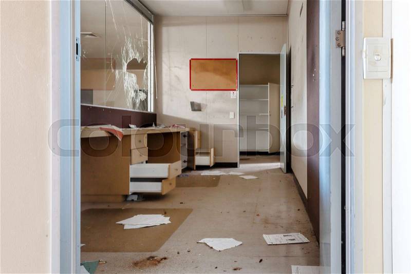 Vandalised reception office area of an abandoned building. Protective glass windows smashed blue tack on walls, drawers and filing cabinets left open, paper on ..., stock photo