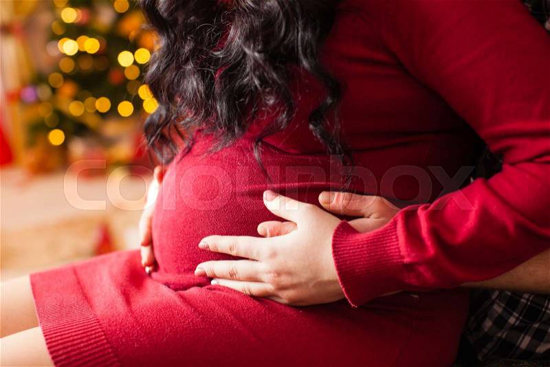 Young pregnant woman and happy father near the blurred decorated Christmas tree, stock photo
