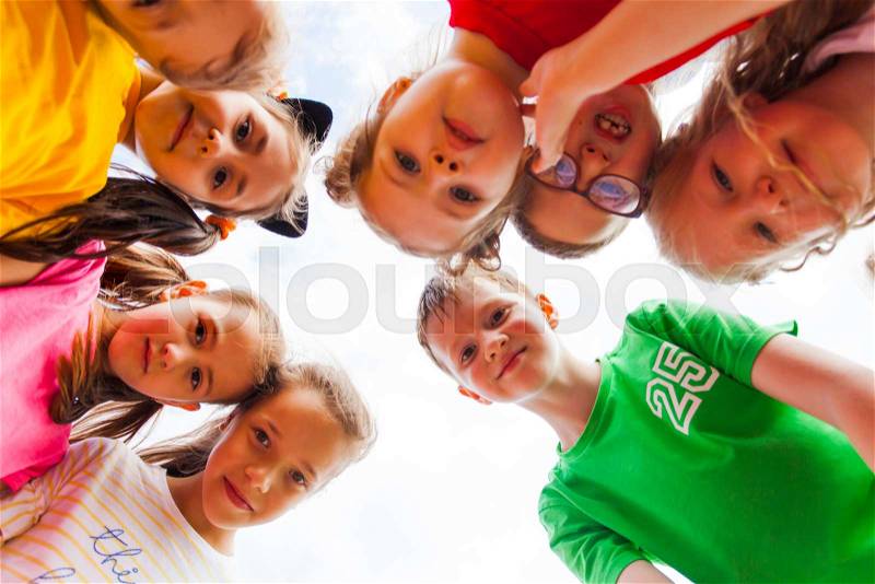 Close view of happy children faces in a circle, bottom view. Eight curious kids looking at the camera, standing in a circle, stock photo