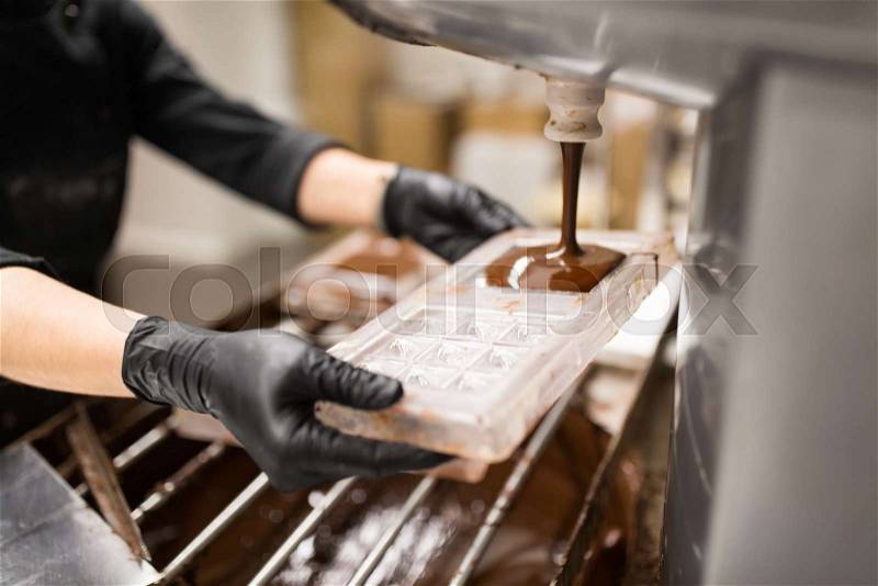 Production, cooking and people concept - confectioner filling candy mold with chocolate at confectionery shop, stock photo