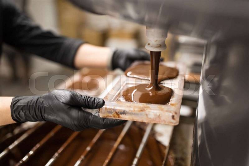 Production, cooking and people concept - confectioner filling candy mold with chocolate at confectionery shop, stock photo
