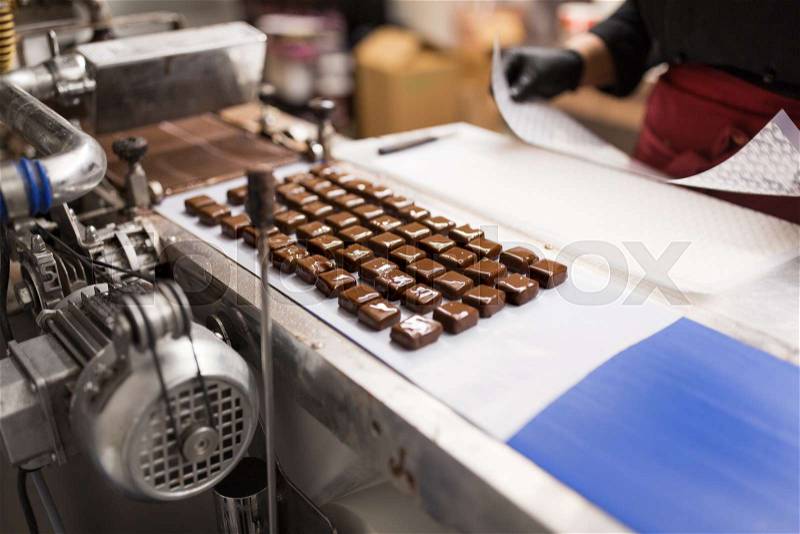 Sweets production and industry concept - chocolate candies processing on conveyor at confectionery shop, stock photo