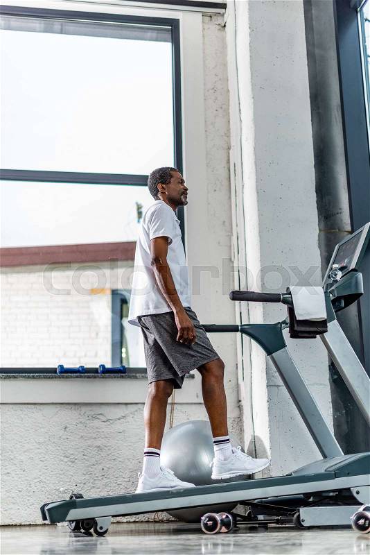 Low angle view of middle aged african american man exercising on treadmill at gym, stock photo