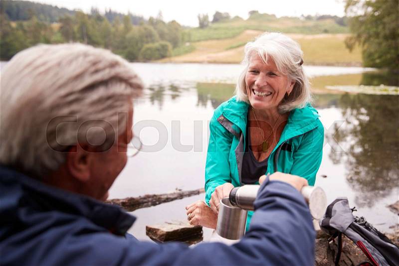 Senior couple by a lake, man pouring coffee to his wifeÕs cup, over shoulder view, Lake District, UK, stock photo