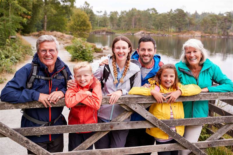 Multi generation family standing behind a wooden fence looking to camera, Lake District, UK, stock photo