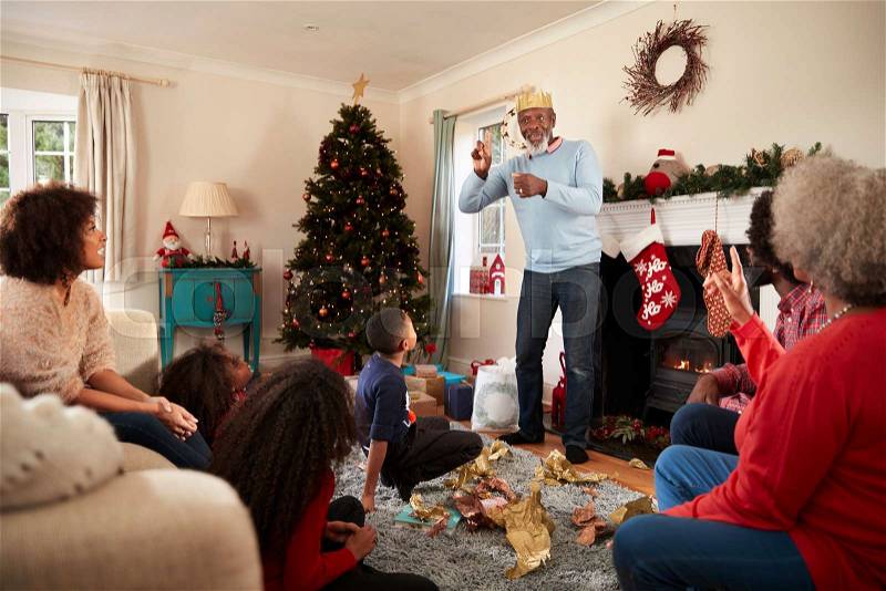 Multi Generation Family Playing Game Of Charades As They Celebrate Christmas At Home Together, stock photo