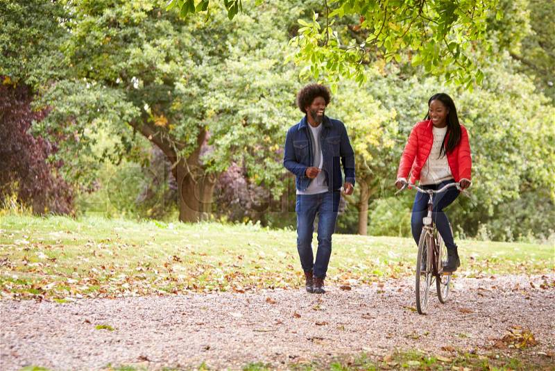 Black couple having fun in a park, the woman riding a bike, front view, stock photo
