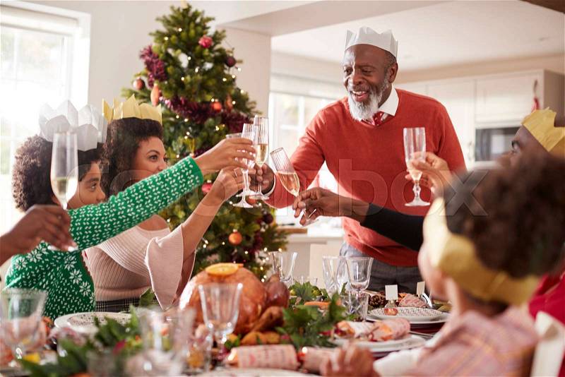 Black grandfather standing to make a toast at the head of the family Christmas dinner table, front view, stock photo
