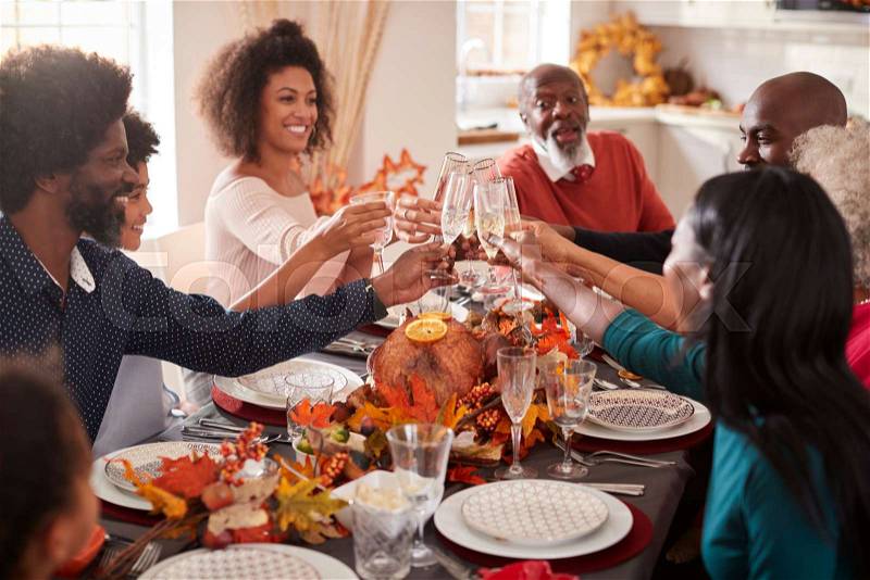Multi generation mixed race family raise their glasses to make a toast at their Thanksgiving dinner table, stock photo