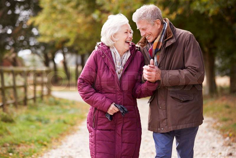 Active Senior Couple On Autumn Walk On Path Through Countryside, stock photo