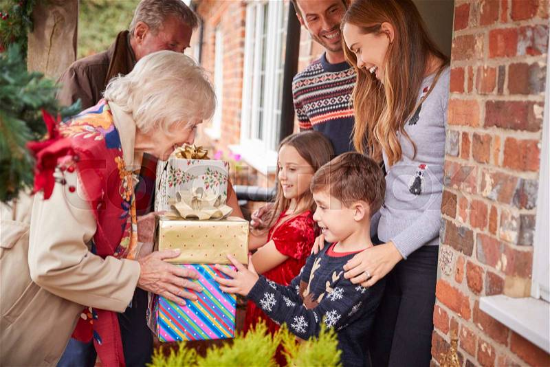 Grandparents Being Greeted By Family As They Arrive For Visit On Christmas Day With Gifts, stock photo