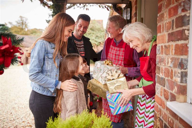 Family Being Greeted By Grandparents As They Arrive For Visit On Christmas Day With Gifts, stock photo
