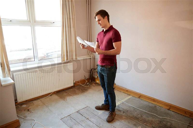 Male First Time Buyer Looking At House Survey In Room To Be Renovated, stock photo