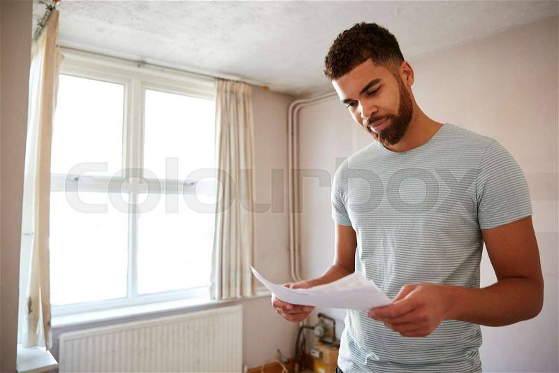 Male First Time Buyer Looking At House Survey In Room To Be Renovated, stock photo