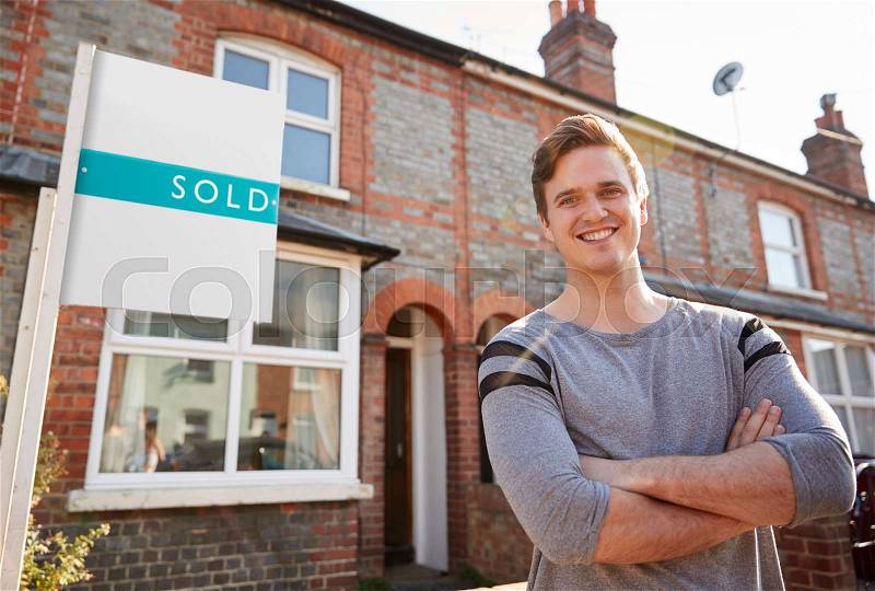 Portrait Of Excited Man Standing Outside New Home With Sold Sign, stock photo