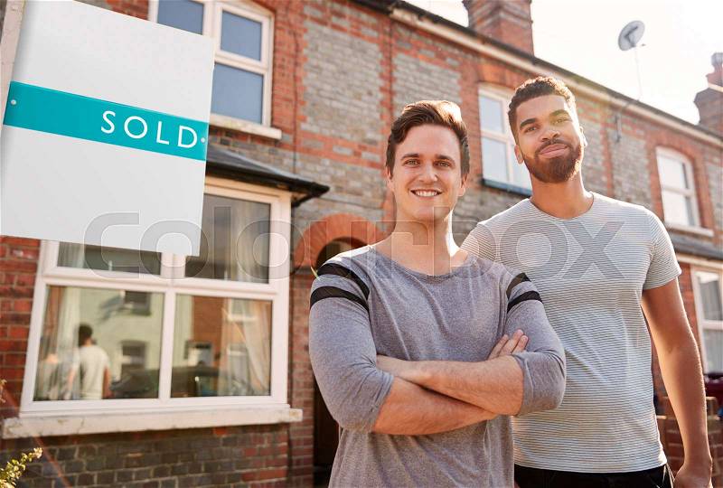 Portrait Of Two Men Standing Outside New Home With Sold Sign, stock photo