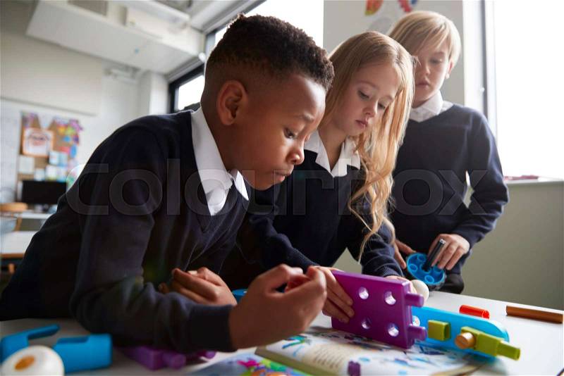 Close up of three primary school children working together with toy construction blocks in a classroom, low angle, side view, stock photo