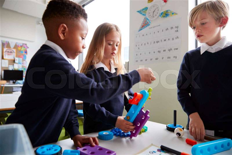 Close up of three primary school children working together with toy construction blocks in a classroom, side view, stock photo
