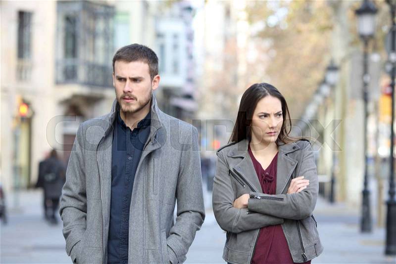 Front view portrait of an angry couple walking in the street after argument, stock photo