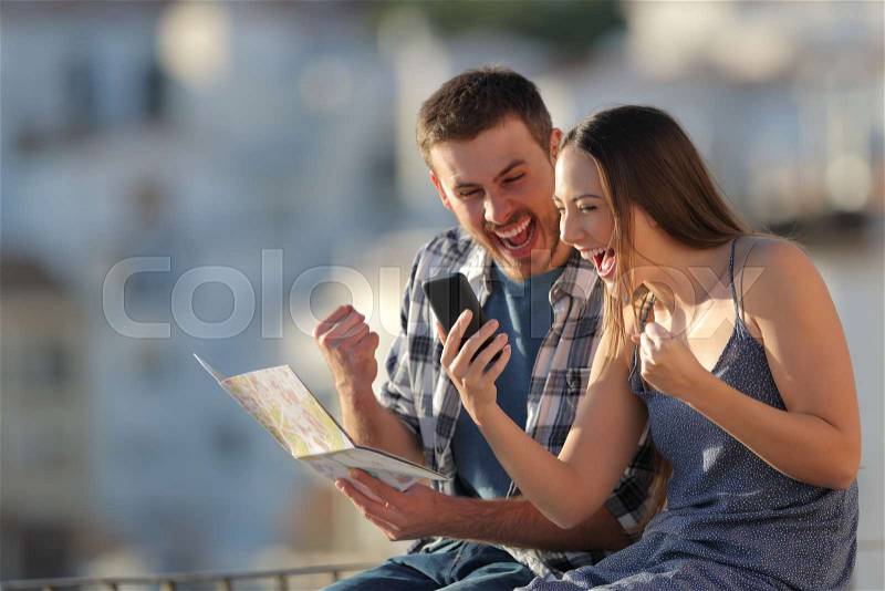 Excited tourists finding best offer on a smart phone sitting on a ledge in a town, stock photo