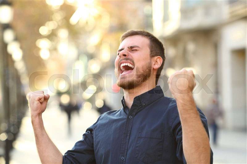 Portrait of an excited guy celebrating success in a city street, stock photo