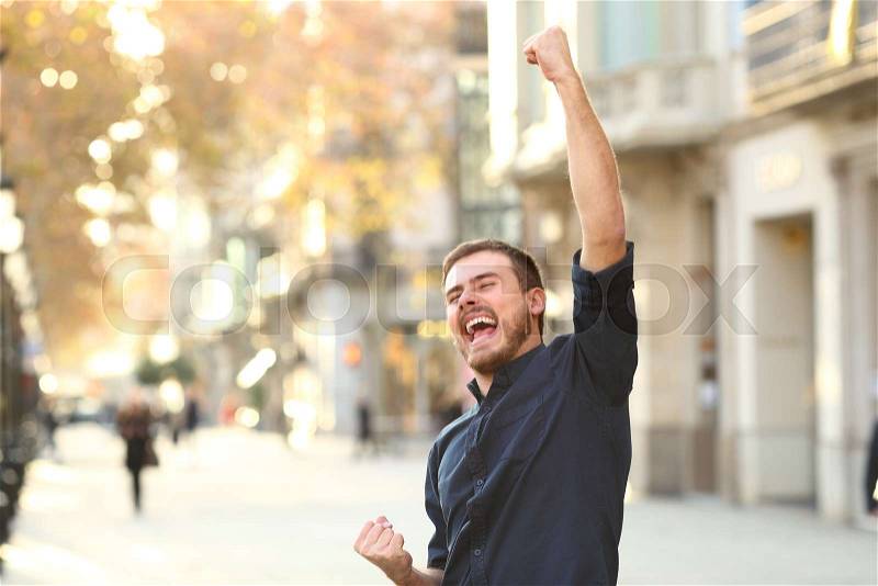 Excited man raising arms celebrating sucess in the middle of the street, stock photo