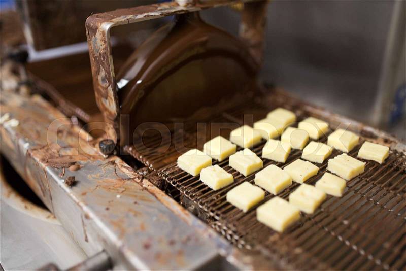 Production, candy shop and industry concept - marzipan bars processing on chocolate coating machine at confectionery, stock photo