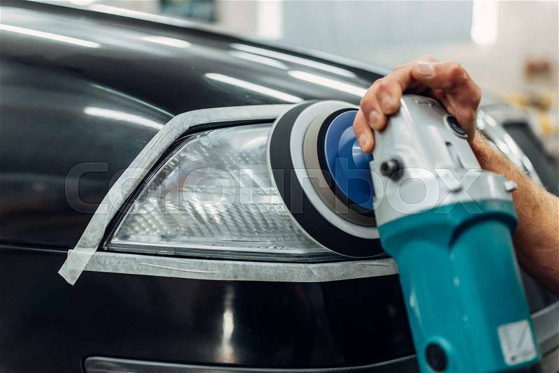 Auto detailing of car headlights on carwash service. Worker cleaning glass with polishing machine, stock photo