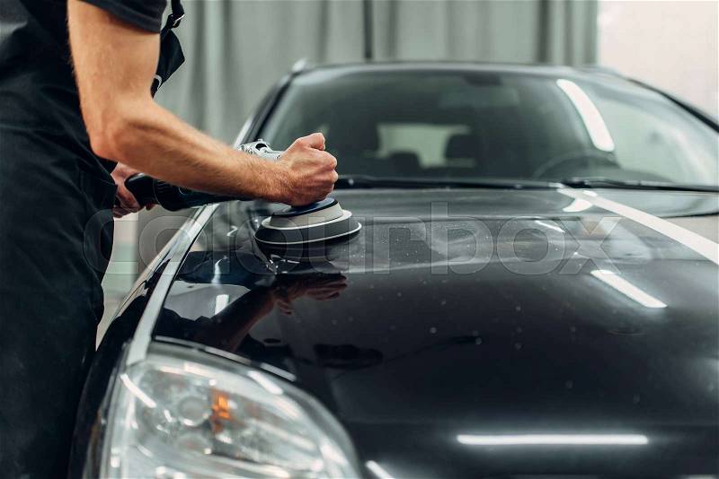 Male person with polishing machine cleans car. Auto detailing on carwash station, restore the paint of vehicle, stock photo