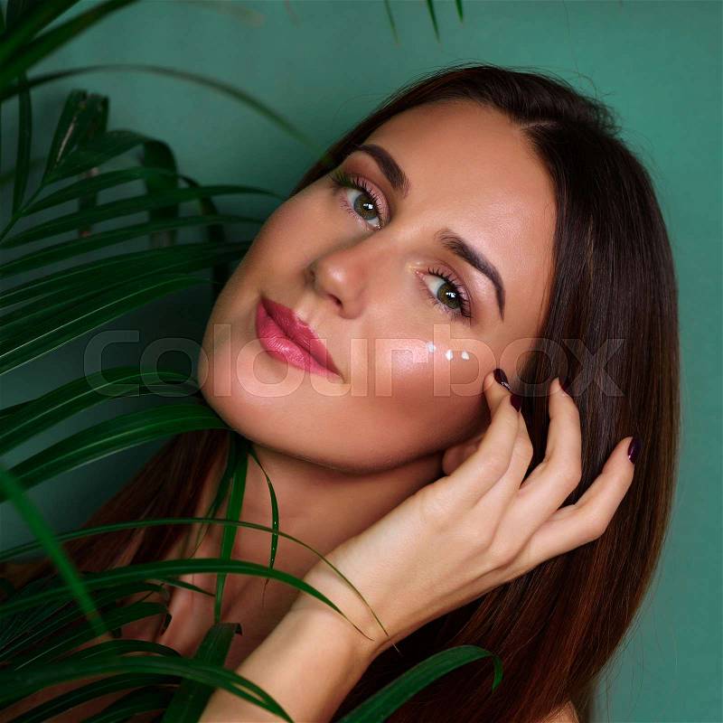 Girl with cream dots on her face between palm leaves on green background. Copy space. Beauty, healthy skin, body care, natural make up concept. Square crop, stock photo