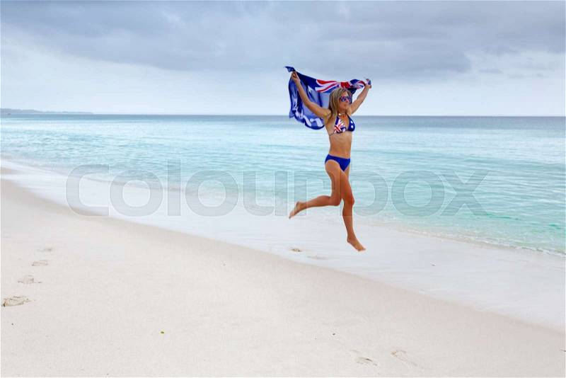 Woman in motion as she runs along the beach holding Australian flag above her Celebrate Australia Day, stock photo
