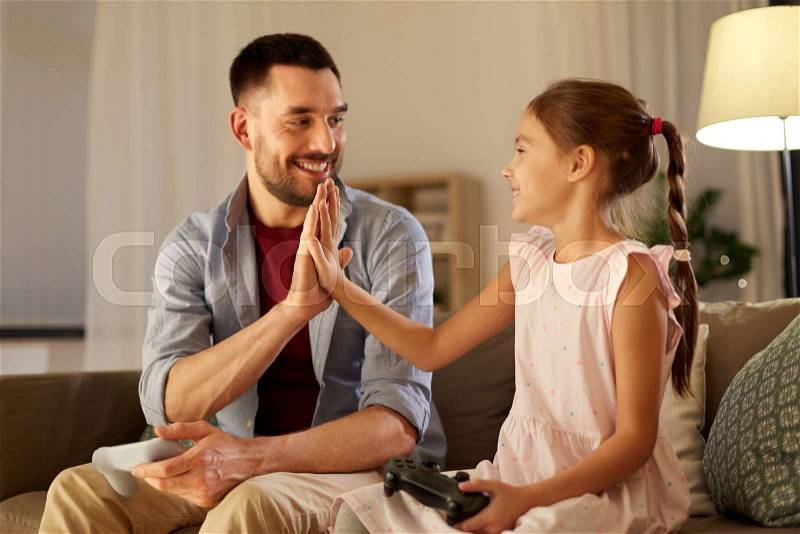 Family, gaming and entertainment concept - happy father and little daughter with gamepads playing video game at home in evening, stock photo