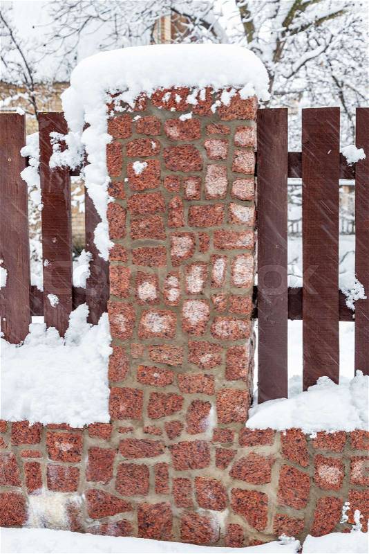 Wooden fence with a stone foundation covered with snow after a heavy snowfall in winter, stock photo