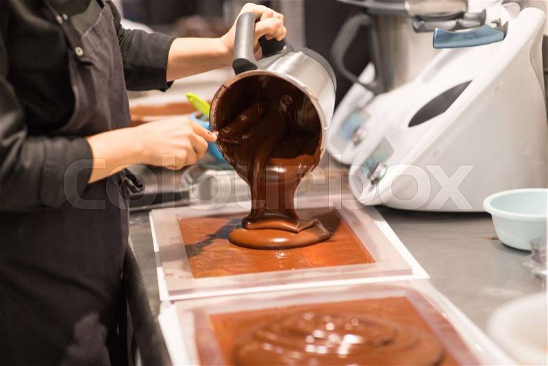 Production, cooking and people concept - confectioner filling mold with chocolate at confectionery shop, stock photo