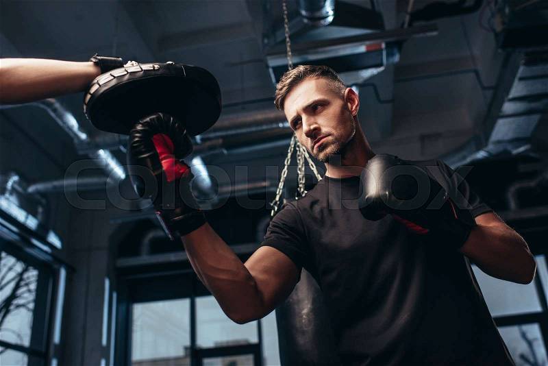Low angle view of handsome boxer exercising with trainer in gym, stock photo