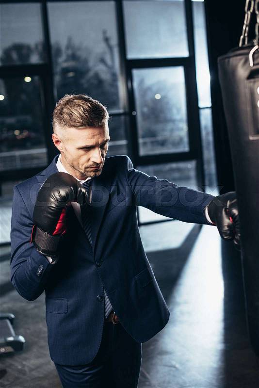 Handsome businessman in suit boxing in gym, stock photo