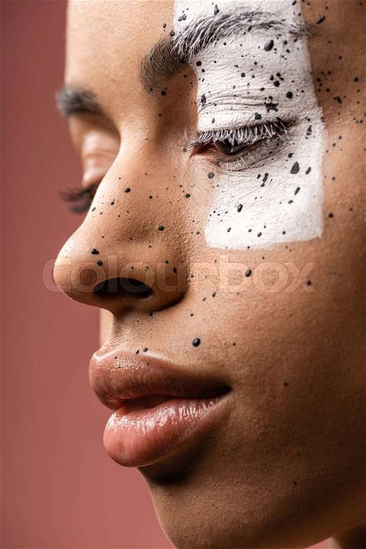 Close-up view of pensive tender african american girl with white paint and brown splashes on face isolated on pink, stock photo