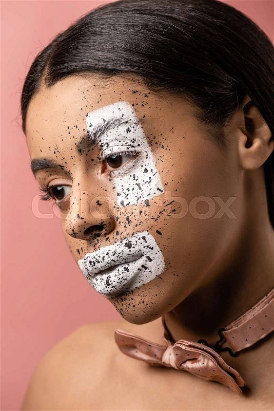 Attractive pensive african american girl with bow tie and paint on face looking away isolated on pink, stock photo