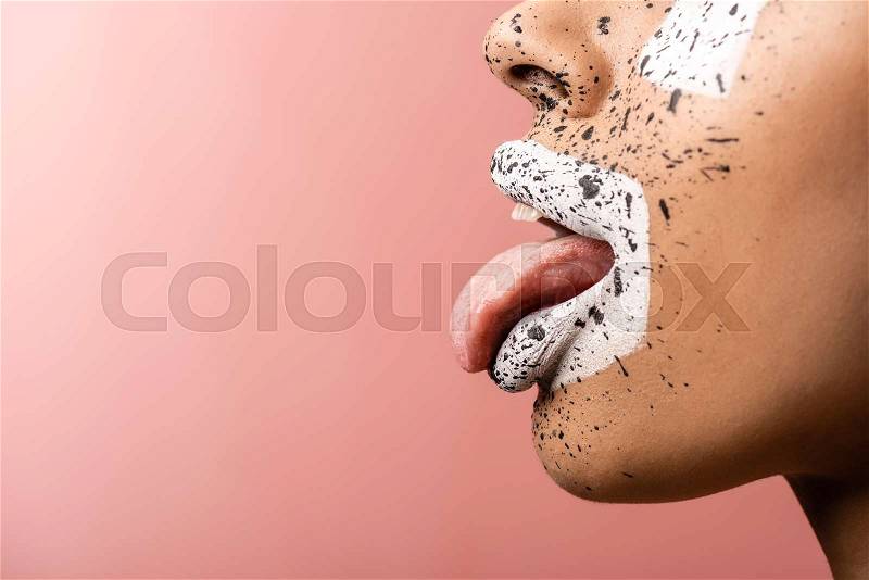 Cropped shot of african american girl with paint splashes on face showing tongue out isolated on pink , stock photo