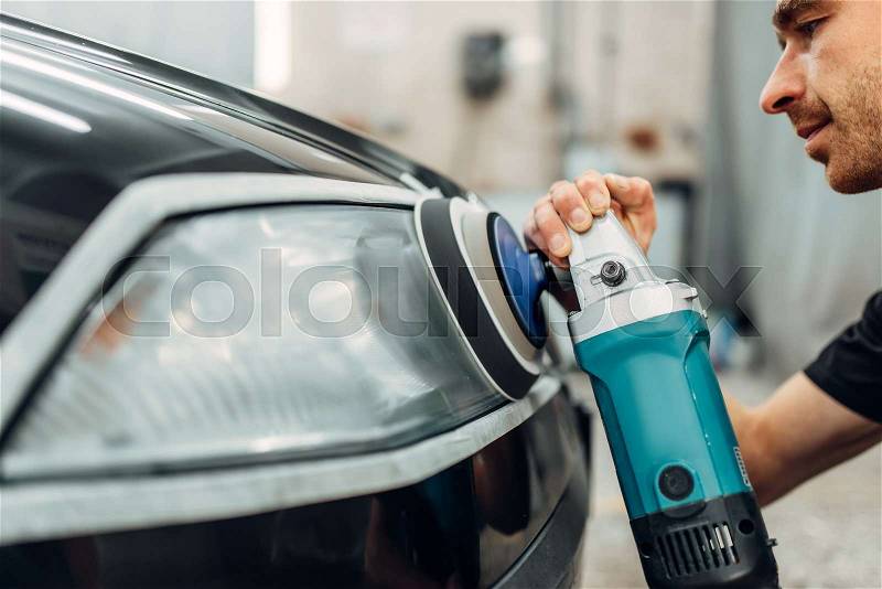 Auto detailing of car headlights on carwash service. Worker cleans glass with polishing machine, stock photo