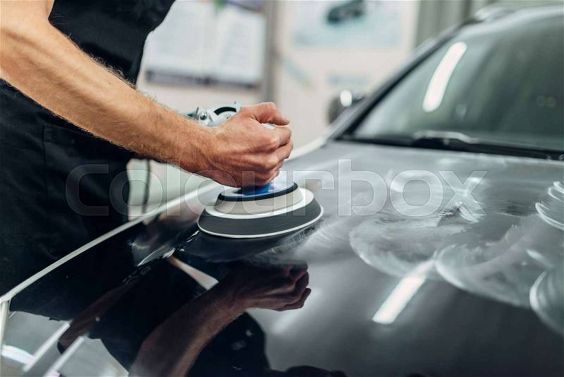 Male person with polishing machine cleans car hood. Auto detailing on carwash service, restore the paint of vehicle, stock photo