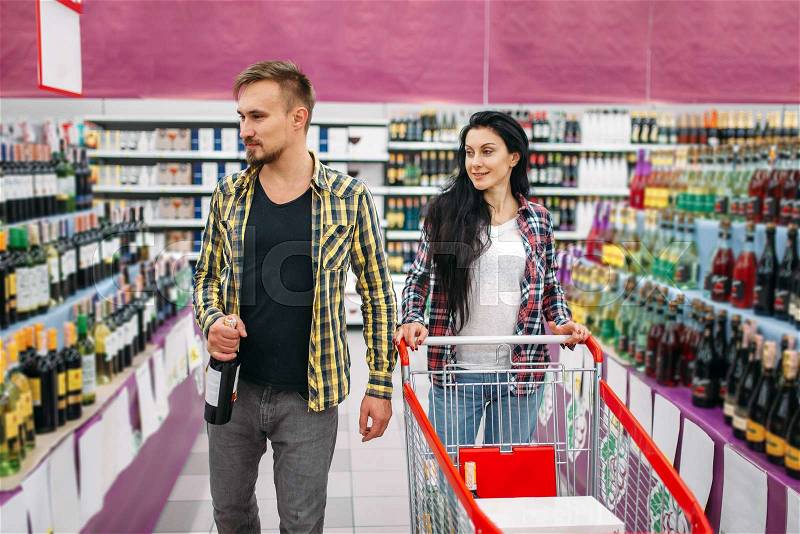 Young couple in supermarket, holiday shopping. Male and female customers buying alcohol. Man and woman purchasing beverages, stock photo