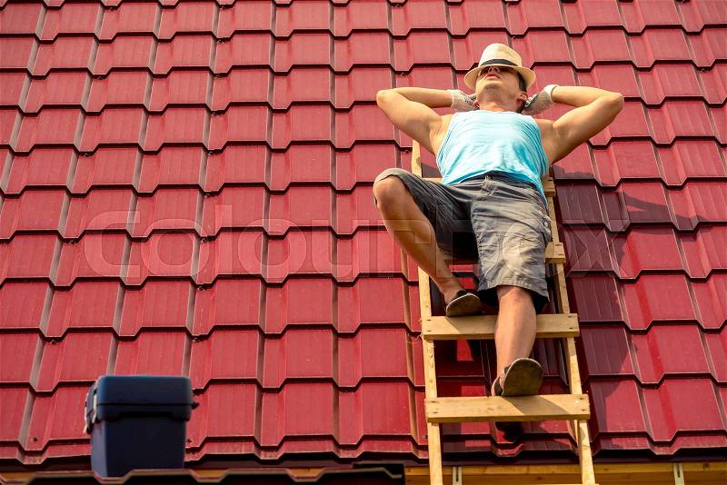 Worker resting in the sun on the stairs on the roof of the house, against the background of tiles, stock photo